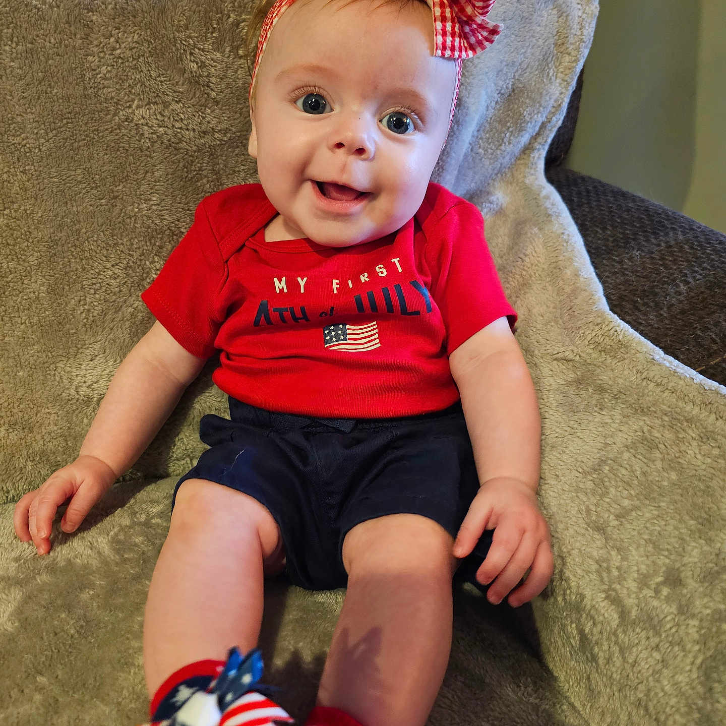Bena is registered to the contest to win money with this photo: baby, blanket, bow, child, clothing, cute, fabric, face, feet, happy, headband, indoor, infant, pattern, person, portrait, red_shirt, sitting, smiling, socks