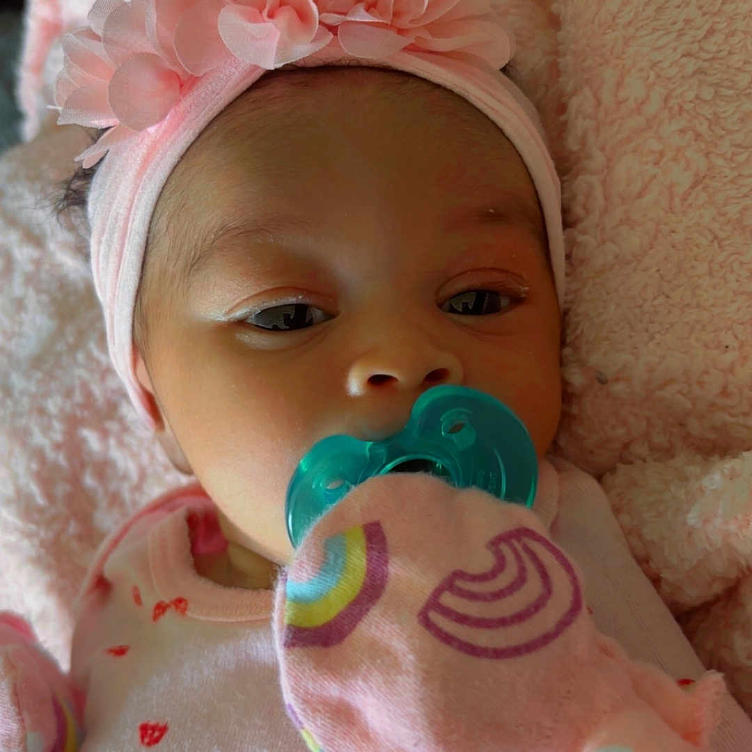 Aliyannah is registered to the contest to win money with this photo: adorable, apparel, baby, blanket, child, closeup, cute, face, hand, headband, infant, lying_down, mittens, newborn, pacifier, pattern, pink, portrait, sleepwear, soft