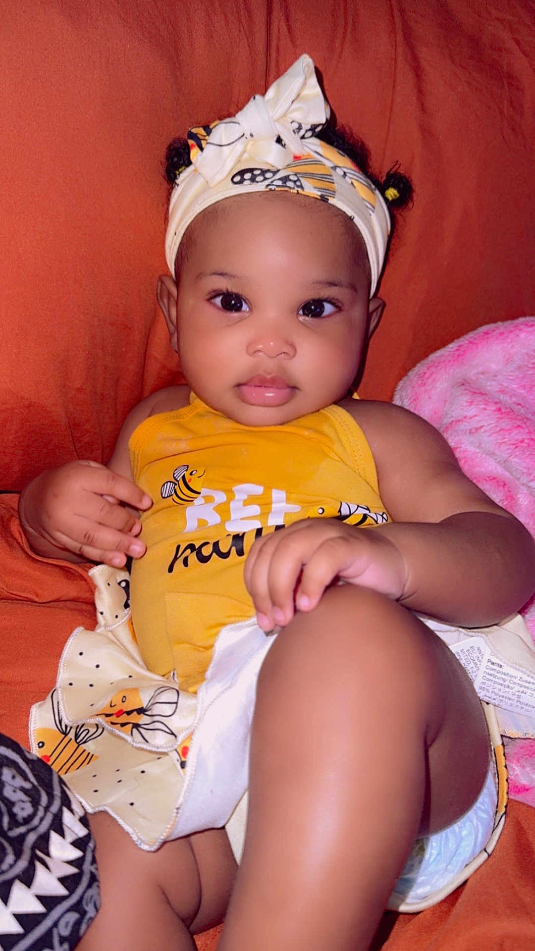 Zuri joined the competition — help win amazing prizes! baby, child, infant, yellow_clothing, headband, bee_pattern, couch, orange_background, pink_blanket, diaper, cute, portrait, indoors, relaxed, small_hands, big_eyes, soft_skin, sitting, looking_at_camera, clothing