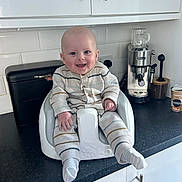 Henry joined the competition — help win amazing prizes! baby, infant, smiling, baby_seat, kitchen, countertop, appliance, coffee_machine, cabinet, white, striped_pajamas, socks, happy, child, person, indoor, furniture, modern, cute, home
