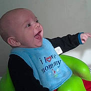Elias joined the competition — help win amazing prizes! arm, baby, bib, bumbo_seat, cheek, clothing, diaper_organizer, ear, face, green_seat, hand, happy, indoor, infant, laughing, portrait, sitting, smiling, text_on_bib, wall