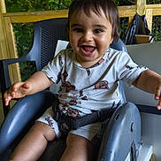 Zakaria a rejoint le concours — aidez-le/la à gagner de superbes lots ! toddler, child, smiling, high_chair, outdoor, greenery, wooden_deck, baby_clothes, happy, cute, arms_outstretched, face, feet, seatbelt, plastic_chair, wood, nature, playful, infant, portrait