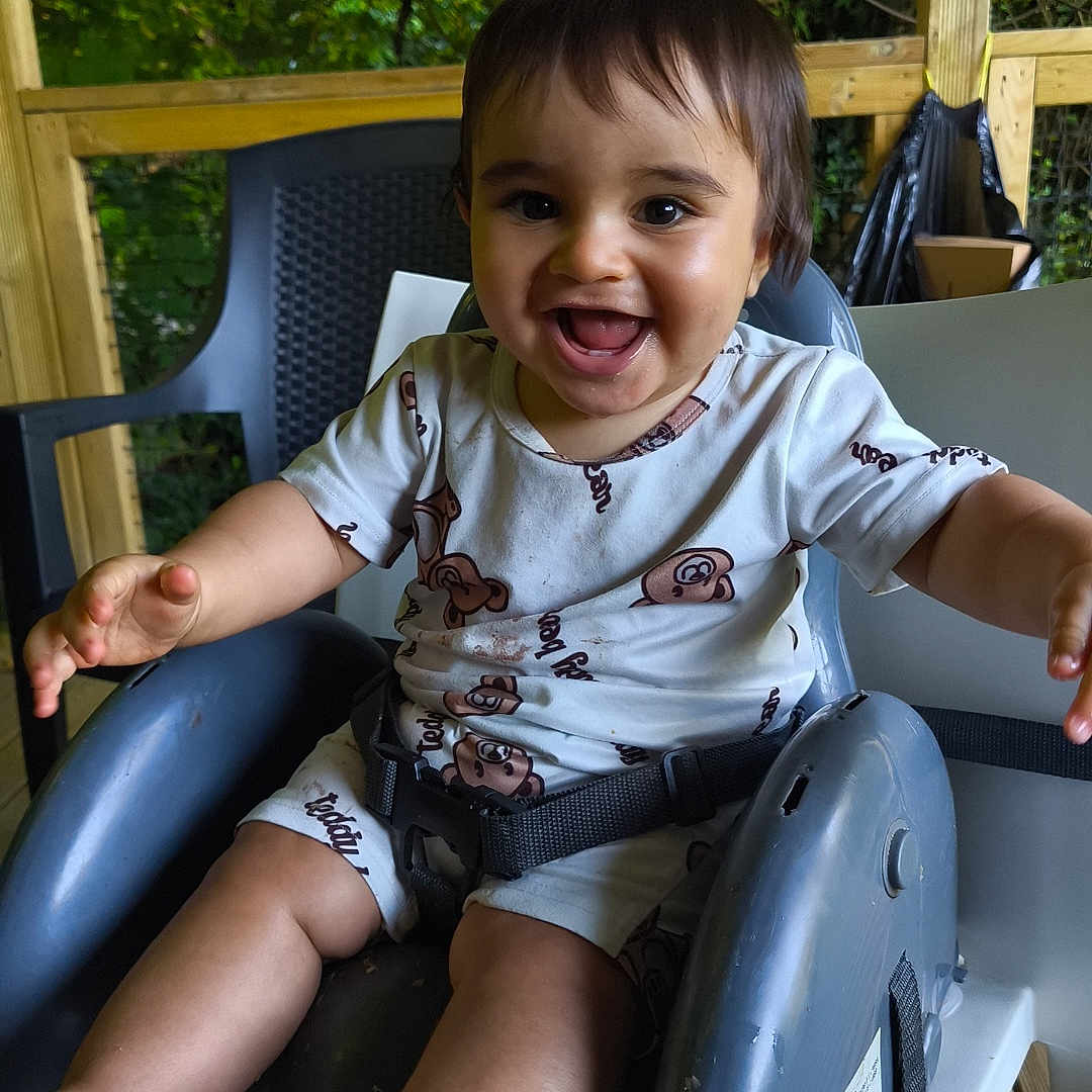 Zakaria a rejoint le concours — aidez-le/la à gagner de superbes lots ! baby, barefoot, child, clothing, cute, daylight, face, greenery, happy, high_chair, leaf, nature, outdoor, person, playful, seatbelt, smiling, toddler, tree, wooden_deck