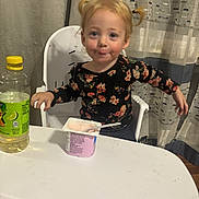 Ellie joined the competition — help win amazing prizes! toddler, child, high_chair, yogurt, food, drink, bottle, table, curtain, indoor, face, smile, pigtails, floral_clothing, messy, person, young_child, happy, kitchen, snack