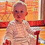 Milo participe au concours pour gagner de l'argent avec cette photo : baby, child, pajamas, indoor, toy, play_mat, floor, window, curtains, sunlight, red_strap, colorful, expression, sitting, hand, face, blue_eyes, necklace, wood_floor, home