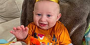 Milo participe au concours pour gagner de l'argent avec cette photo : baby, child, crown, orange_shirt, smiling, happy, toy, plush_toy, indoor, chair, blanket, face, hand, cute, infant, sitting, blue_eyes, wall, home, cozy