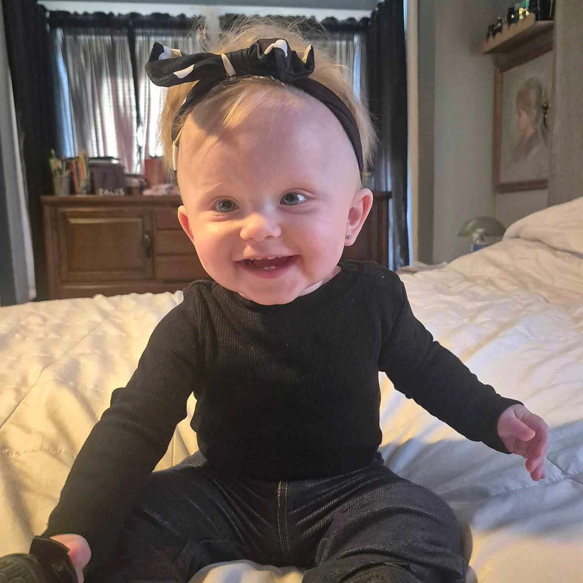 Harmony Reye Lane is registered to the contest to win money with this photo: baby, child, smiling, headband, black_clothing, sitting, bed, indoor, happy, portrait, infant, cute, person, footwear, jeans, room, furniture, curtains, light, home
