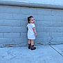 Madeline is registered to the contest to win money with this photo: toddler, child, smile, dress, boots, cowboy_boots, side_view, concrete, brick_wall, outdoor, curly_hair, person, young_child, urban, casual_clothing, standing, looking_back, playful, daylight, innocence