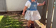 Madeline joined the competition — help win amazing prizes! child, toddler, outdoor, grass, fence, denim, dress, boots, curly_hair, sunlight, shadow, exploring, happy, person, nature, wood, playful, young, smiling, daylight