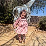 toddler, child, girl, pink_dress, cowboy_boots, mosaic_giraffe, sculpture, outdoor, sunny, wooden_path, plants, trees, shadows, curly_hair, hair_bow, nature, daylight, playful, cute, portrait