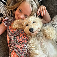 Lucy joined the competition — help win amazing prizes! child, dog, cuddling, smiling, curly_hair, patterned_clothing, couch, cushion, indoor, happy, relaxed, blond_hair, pet, friendship, portrait, closeup, hand, resting, cozy, casual