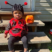 Milani joined the competition — help win amazing prizes! child, costume, ladybug, pumpkin, jackolantern, steps, outdoor, sunlight, black, red, hat, shoes, wood, person, fall, halloween, cute, expression, sitting, holiday