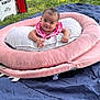 baby, infant, pink_clothing, smiling, face, outdoor, grass, blanket, cushion, pillow, cooler, toy, child, happy, lying_down, nature, relaxing, cute, people, daylight