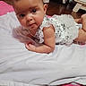 baby, infant, child, portrait, tummy_time, lying_down, white_dress, frills, blanket, bed, pink_blanket, indoors, home, wood_floor, furniture, monitor, bottle, face, wide_eyed, photography
