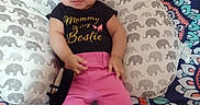 Kodiana joined the competition — help win amazing prizes! baby, child, infant, sitting, portrait, smiling, face, eyes, pink_pants, black_shirt, clothing, pillow, elephant_pattern, bed, blanket, indoors, colorful, text_on_clothing, family, cute