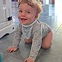 animal_print, baby, bib, blue_eyes, cabinet, child, crawling, curly_hair, cute, floor, happy, indoor, light, long_sleeve_shirt, person, playful, smiling, tile_floor, toddler, young_child