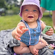 Judith a rejoint le concours — aidez-le/la à gagner de superbes lots ! baby, child, blue_eyes, hat, outdoor, grass, blanket, toy, smiling, happy, summer, play, sitting, cute, infant, person, clothing, hand, foot, daylight