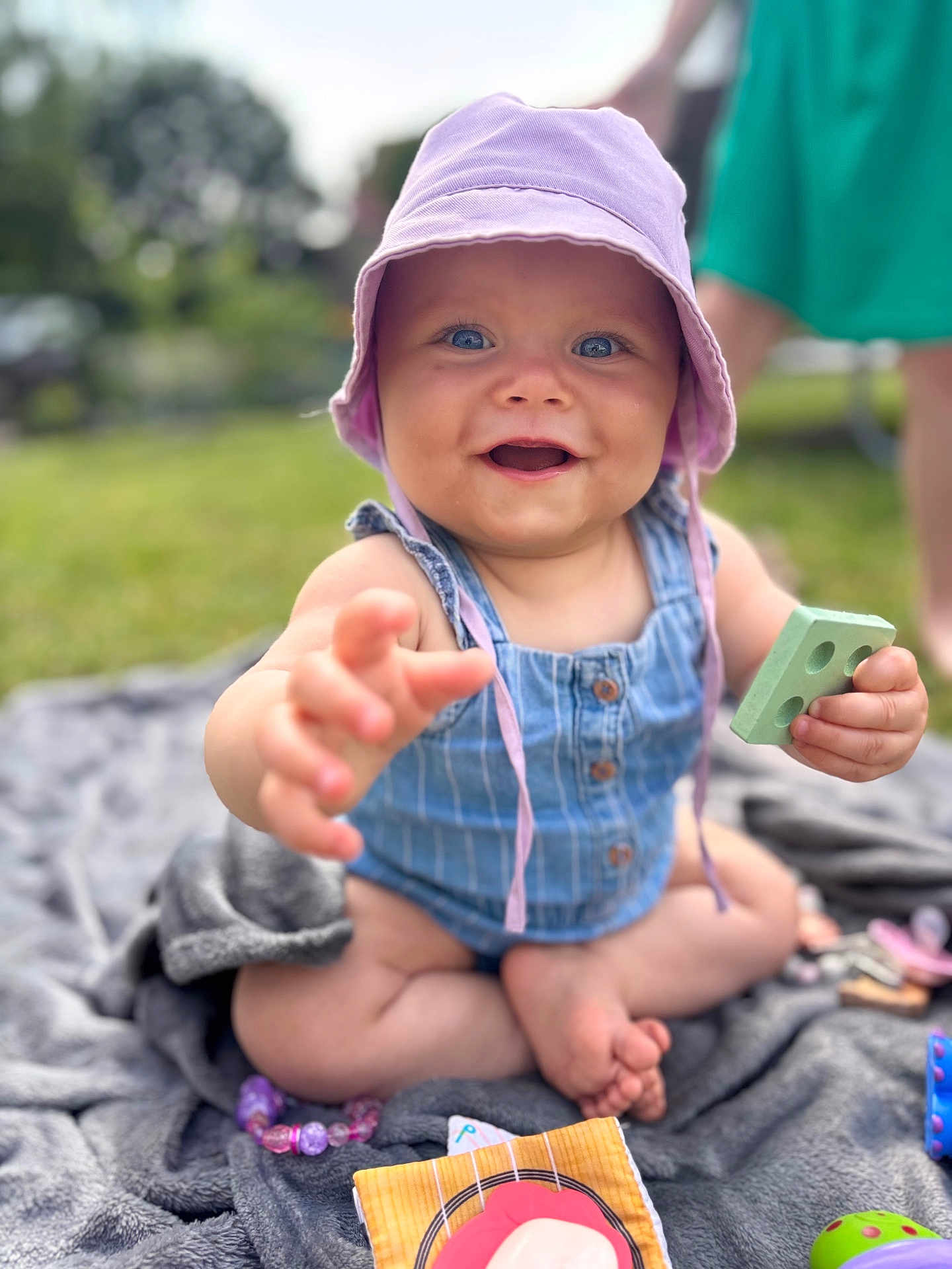 Judith a rejoint le concours — aidez-le/la à gagner de superbes lots ! baby, child, blue_eyes, hat, outdoor, grass, blanket, toy, smiling, happy, summer, play, sitting, cute, infant, person, clothing, hand, foot, daylight