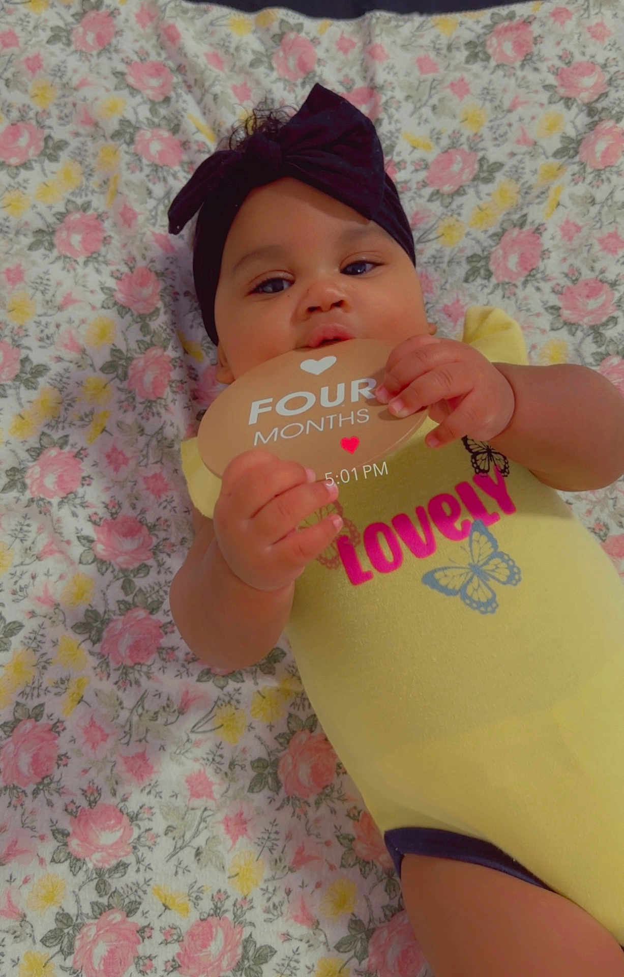 Camiyah is registered to the contest to win money with this photo: baby, infant, child, headband, yellow_onesie, butterfly, milestone_card, floral_blanket, lying_down, cute, hands, face, smiling, skin, portrait, closeup, indoors, baby_girl, soft_lighting, adorable