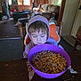 breakfast, carpet, casual, cereal, chair, child, curtain, deer_mount, food, hoodie, indoor, living_room, person, purple_bowl, snack, sofa, table, toys, window, wooden_table