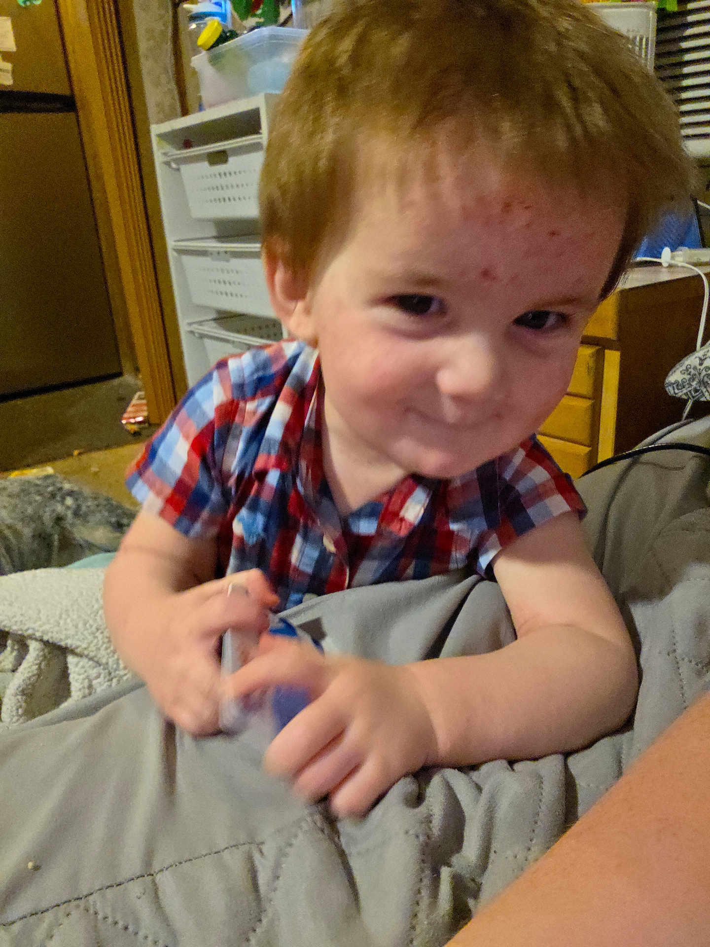 Samuel joined the competition — help win amazing prizes! child, boy, plaid_shirt, indoor, smile, face, hands, blanket, furniture, cabinet, drawer, toy, room, skin, hair, person, playful, young, casual, candid