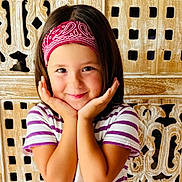 Milla a rejoint le concours — aidez-le/la à gagner de superbes lots ! child, smiling, bandana, striped_shirt, portrait, happy, cute, hands_on_face, wooden_background, short_hair, indoors, person, face, young, playful, posing, casual_clothing, headband, childhood, bright
