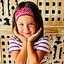 child, smiling, bandana, striped_shirt, portrait, happy, cute, hands_on_face, wooden_background, short_hair, indoors, person, face, young, playful, posing, casual_clothing, headband, childhood, bright