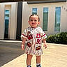 child, toddler, outdoor, sunlight, building, window, clothing, sneakers, smiling, person, concrete, shadow, greenery, shorts, shirt, happy, daylight, street, urban, portrait