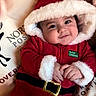 baby, child, smile, santa_outfit, hood, red_clothing, holiday, christmas, festive, pillow, reindeer, cute, face, hands, indoors, soft_texture, plush, cozy, infant, portrait