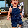 toddler, child, denim_overalls, smiling, white_sneakers, outdoor, stone_patio, happy, face, person, walking, shorts, casual_clothing, young_child, cute, small_hands, home, blurred_background, daylight, portrait