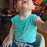 baby, blue_eyes, child, clothing, colorful_background, curious, expression, face, hand, high_chair, indoor, neon_lights, person, polka_dot_pants, portrait, restaurant, seat_belt, sitting, toddler, turquoise_shirt