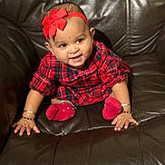 Jisha joined the competition — help win amazing prizes! baby, child, red_bow, headband, plaid_dress, red_socks, bracelets, smiling, leather_couch, brown_couch, happy, cute, portrait, sitting, infant, indoors, person, furniture, young_child, adorable