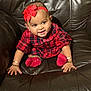 baby, child, red_bow, headband, plaid_dress, red_socks, bracelets, smiling, leather_couch, brown_couch, happy, cute, portrait, sitting, infant, indoors, person, furniture, young_child, adorable