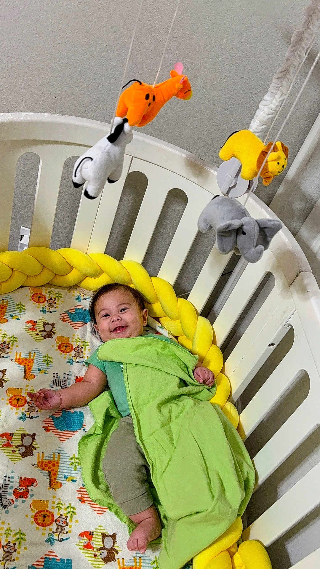 Patrick joined the competition — help win amazing prizes! baby, crib, blanket, bedding, stuffed_animals, mobile, yellow, green, smiling, child, infant, cute, playful, indoor, furniture, happy, animal_print, toddler, resting, bedroom