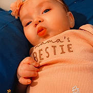 Brielle joined the competition — help win amazing prizes! baby, infant, headband, flower_headband, onesie, text_on_clothing, hand, fingers, pillow, blue_bed, close_up, portrait, cute, lip_pout, skin, lying_down, floral_pants, timestamp, sticker, soft_lighting