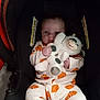 Daxton is registered to the contest to win money with this photo: baby, infant, car_seat, stuffed_animal, plush_toy, onesie, pumpkin_print, child, cute, sitting, indoors, person, face, hands, clothing, toy, seat_belt, warning_label, portrait, young_child