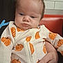 baby, child, infant, pumpkin_pattern, onesie, clothing, hand, person, face, indoor, holding, seated, expression, head, skin, table, background, tile_wall, orange_booth, casual