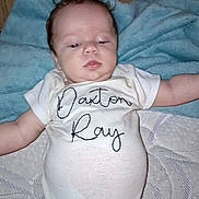 Daxton joined the competition — help win amazing prizes! baby, infant, onesie, blanket, wooden_wall, lying_down, face, head, arm, diaper, soft_surface, clothing, child, person, sleepwear, indoor, newborn, cute, portrait, resting