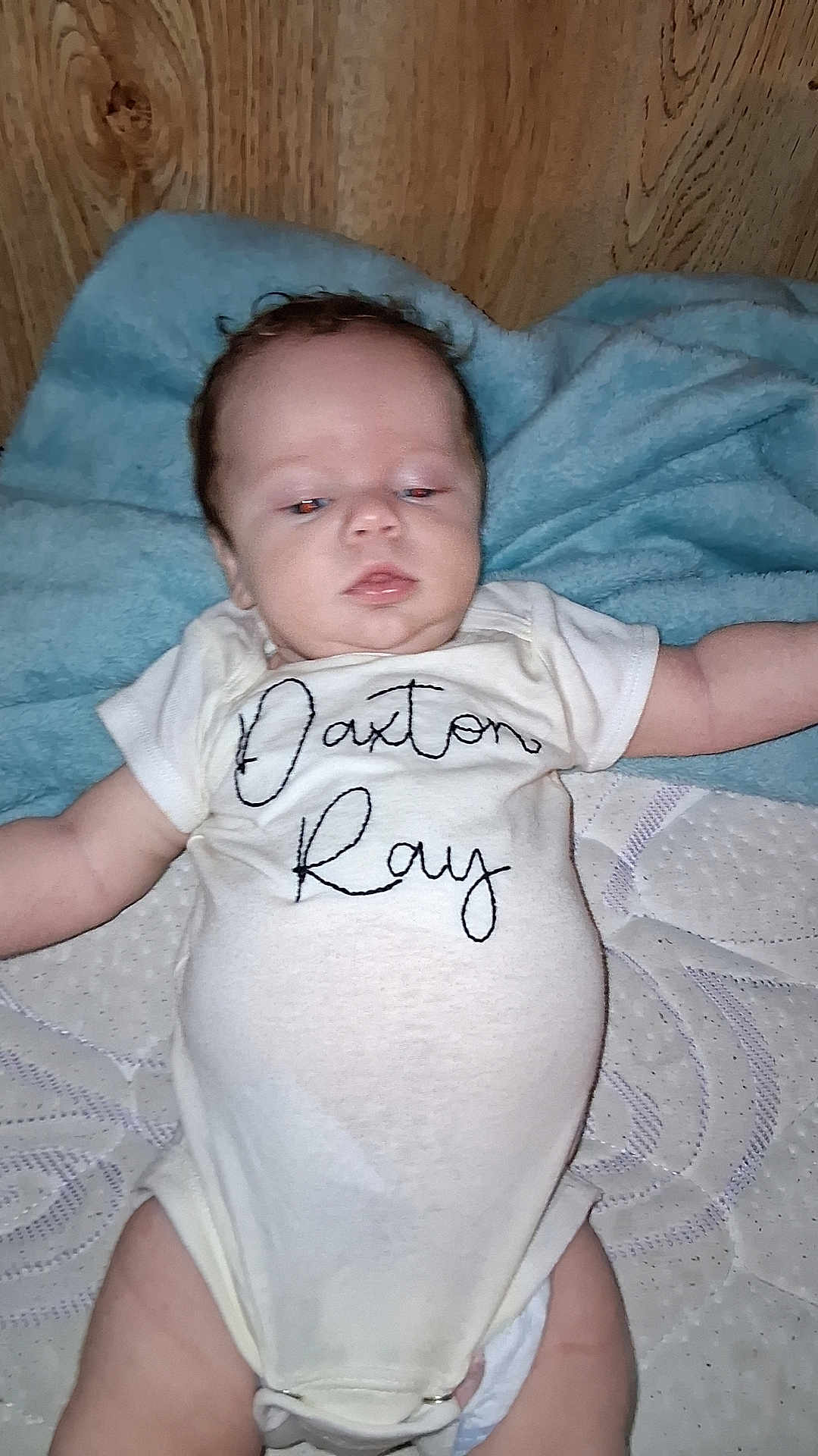 Daxton joined the competition — help win amazing prizes! baby, infant, onesie, blanket, wooden_wall, lying_down, face, head, arm, diaper, soft_surface, clothing, child, person, sleepwear, indoor, newborn, cute, portrait, resting