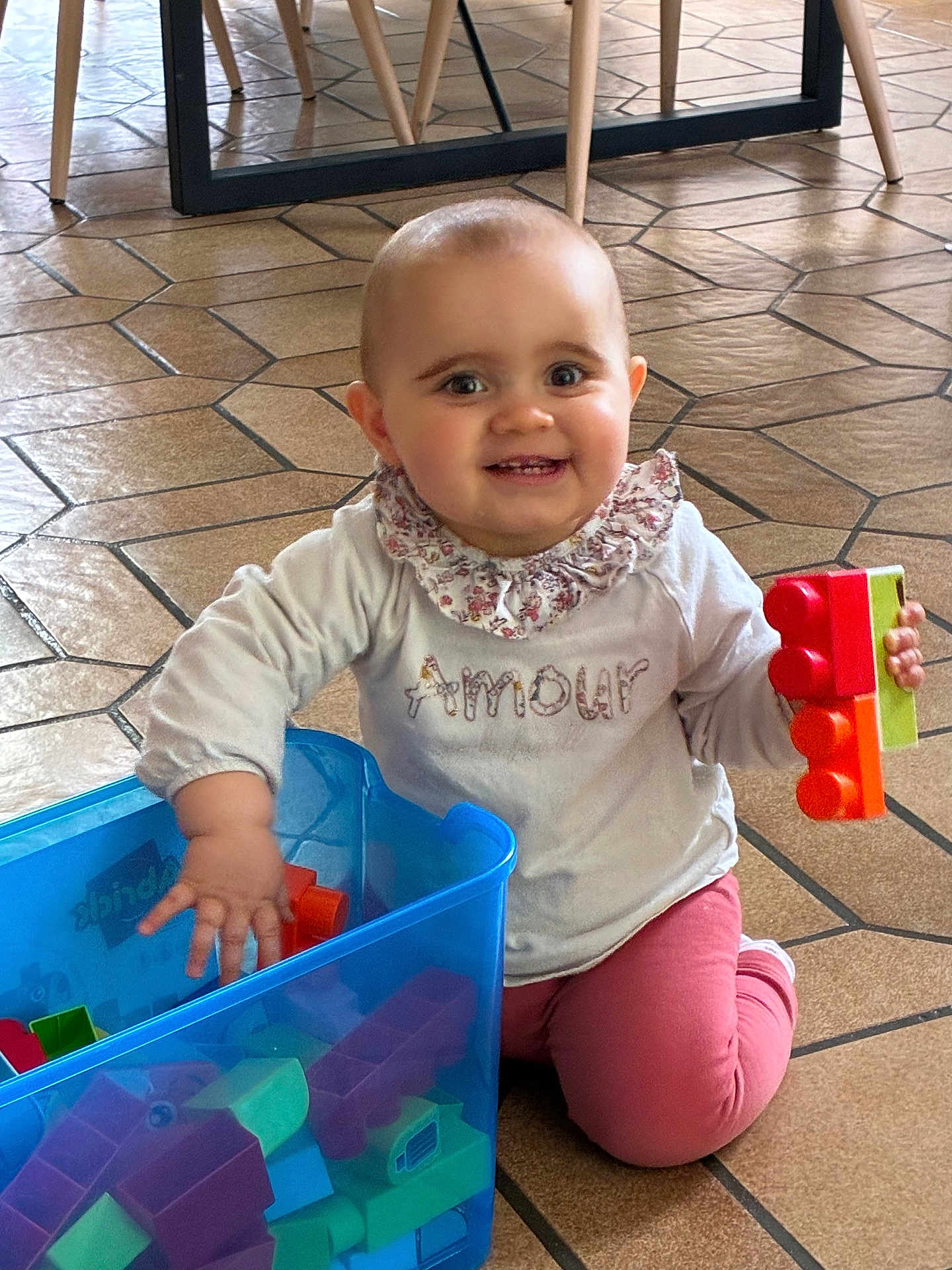Victoire a rejoint le concours — aidez-le/la à gagner de superbes lots ! baby, child, smiling, playing, toys, building_blocks, floor, indoor, container, colorful, clothing, person, happy, cute, face, head, kneeling, toy_blocks, pink_pants, white_shirt