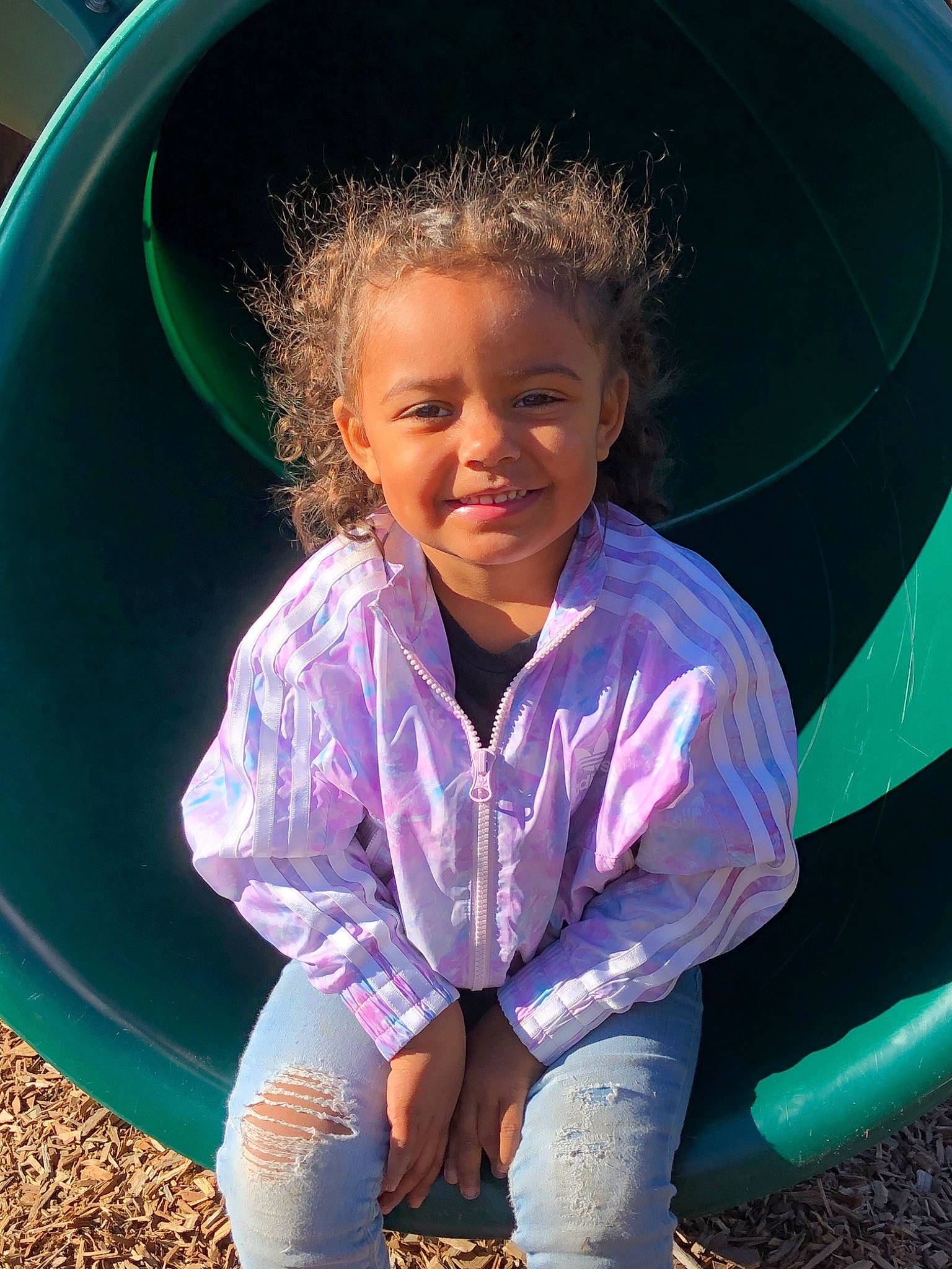 Aniyah joined the competition — help win amazing prizes! blue, child, cool, eye, face, facial_expression, fun, grass, happy, joy, outdoor_play_equipment, people, person, pink, play, playground, public_space, purple, sitting, smile
