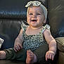 baby, smiling, headband, green_pants, sitting, leather_couch, happy, child, infant, cute, portrait, indoors, young_child, clothing, foot, hand, face, person, furniture, head
