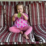 Serenity is registered to the contest to win money with this photo: barefoot, blonde_hair, child, couch, daylight, face, floral_shirt, home, leaf, nature, outdoor, pink_pants, playful, portrait, sitting, smiling, striped_cushion, toddler, window, wooden_floor