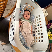 Xavier joined the competition — help win amazing prizes! baby, laundry_basket, blanket, table, chair, floor_tiles, indoor, person, child, face, looking_up, wooden_furniture, household, cushion, curious, cozy, toddler, clothing, domestic, resting