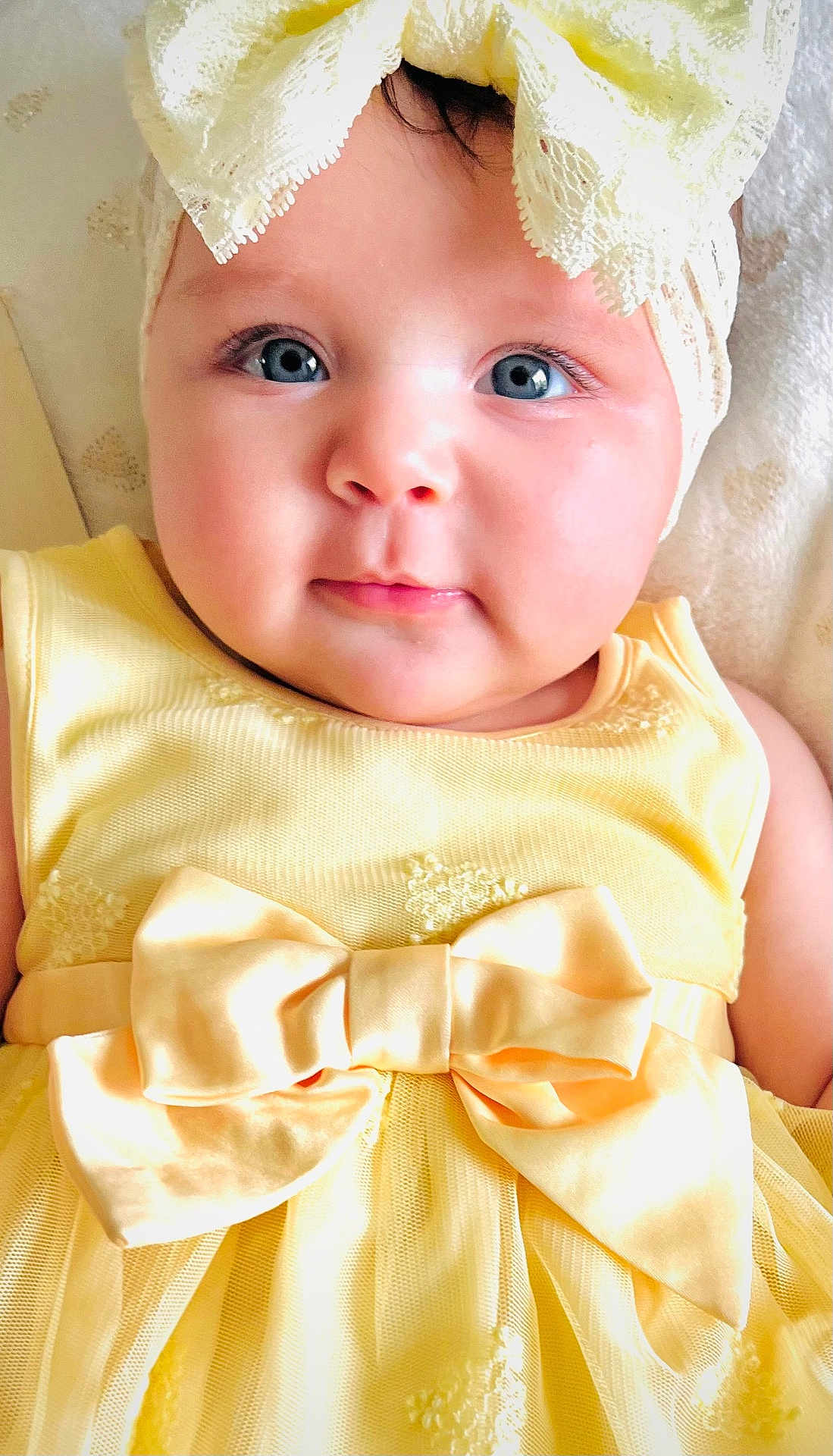 Liz Angeli is registered to the contest to win money with this photo: baby, child, face, blue_eyes, yellow_dress, bow, headband, lace, closeup, portrait, infant, cute, smile, soft_lighting, indoors, skin, adorable, person, young, expression