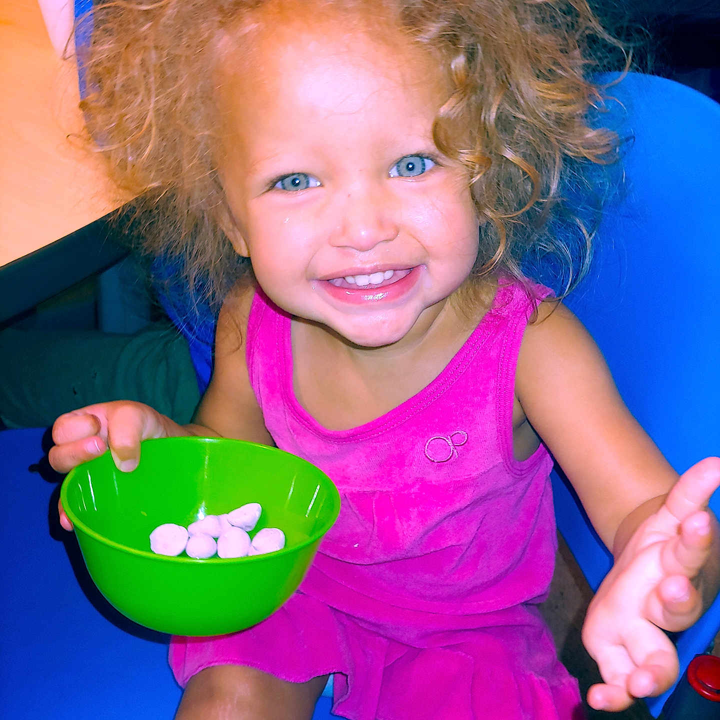 Je'Lani is registered to the contest to win money with this photo: blue_chair, blue_eyes, bright_colors, child, curly_hair, cute, face, food, green_bowl, hand, happy, indoor, person, pink_dress, playing, portrait, sitting, smiling, snacks, toddler