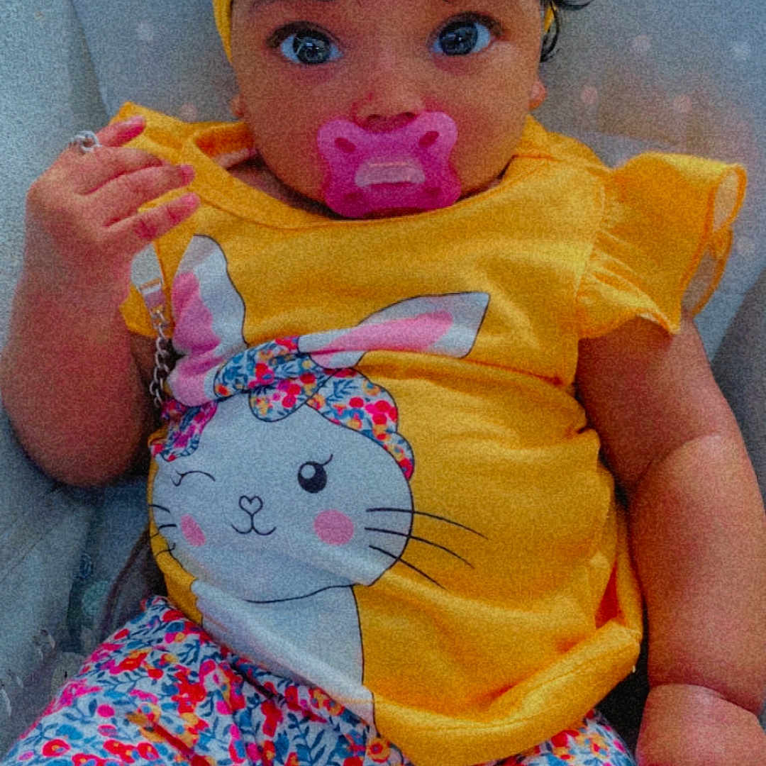 Lena a rejoint le concours — aidez-le/la à gagner de superbes lots ! baby, chair, child, colorful, comfort, cute, expression, floral_pants, headband, headwear, indoors, infant, looking_at_camera, pacifier, patterned_clothing, pink_pacifier, portrait, sitting, yellow_clothing, young_child