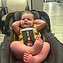 baby, car_seat, child, indoor, person, infant, floor, chair, hallway, relaxing, casual_clothing, foot, hand, seatbelt, head, expression, light, room, comfort, furniture