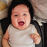 Nicolas is registered to the contest to win money with this photo: baby, smiling, happy, infant, onesie, child, cute, face, person, indoor, cushion, fabric, pattern, skin, head, hand, joy, lying_down, cheerful, dark_hair