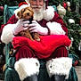 santa_claus, dog, puppy, christmas_tree, christmas_decorations, holiday, festive, red_suit, white_beard, glasses, hat, chair, furry_boots, gloves, indoors, smiling, pet, celebration, pine_cones, red_blanket